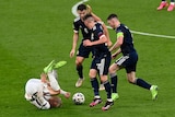 Three Scotland players stand over Phil Foden as he rolls on the ground.