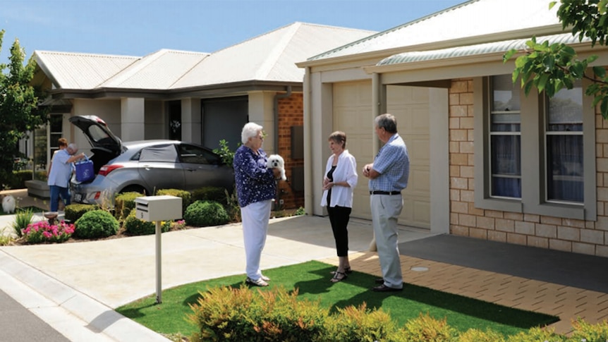 A promotional photograph shows a group of older people chatting in front of a home.
