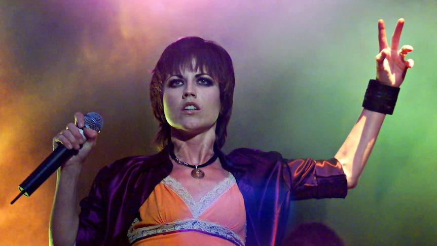The Cranberries lead singer Dolores O'Riordan holds her hand up while on stage.
