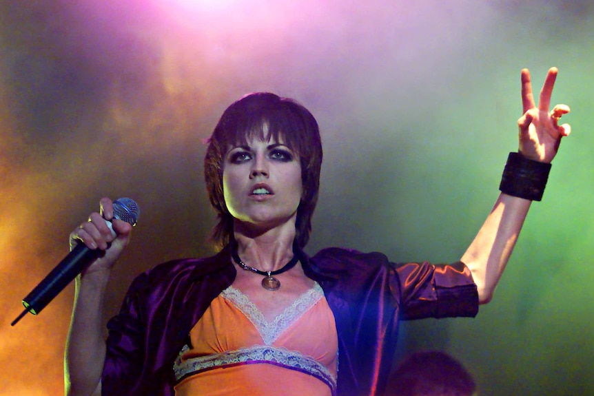 The Cranberries lead singer Dolores O'Riordan holds her hand up while on stage.