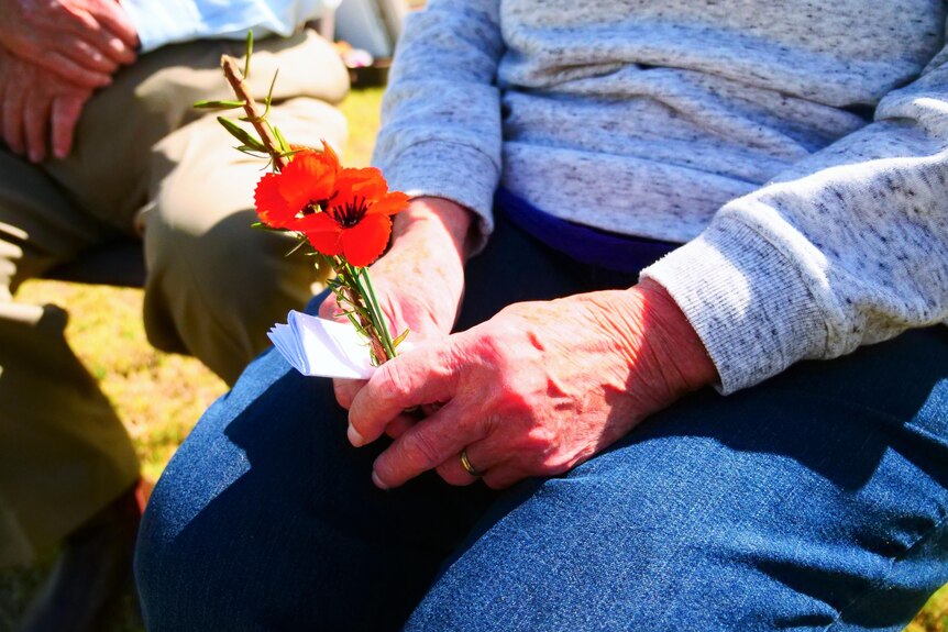 Woman holds red poppy in hands.