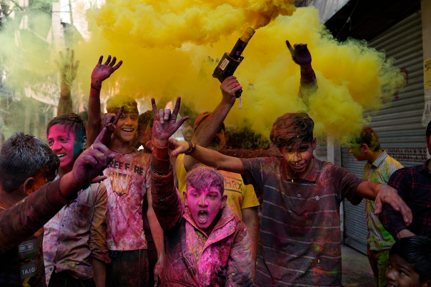 Children covered in coloured powder are walking towards the camera with a cloud of yellow powder above them.