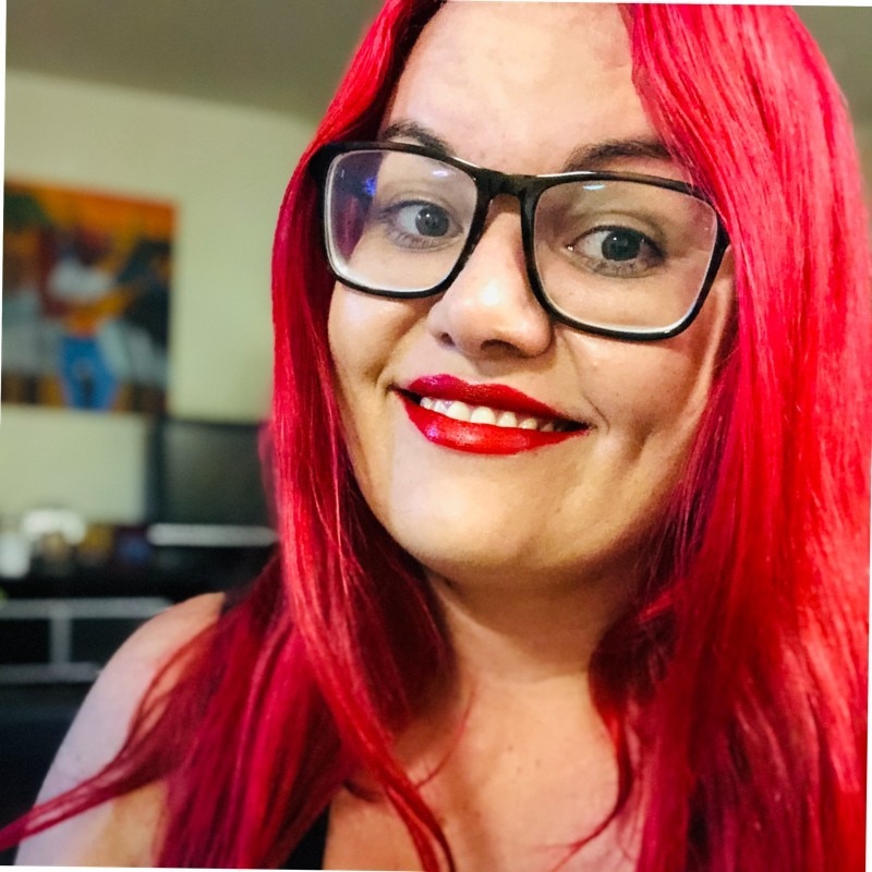 A close-up shot of a First Nations woman with dyed red hair and glasses
