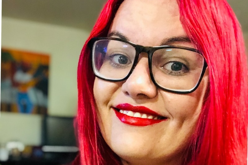 A close-up shot of a First Nations woman with dyed red hair and glasses