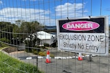 A warning sign hangs on a fence out the front of a landslip-damaged property