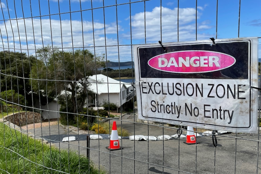 A warning sign hangs on a fence out the front of a landslip-damaged property