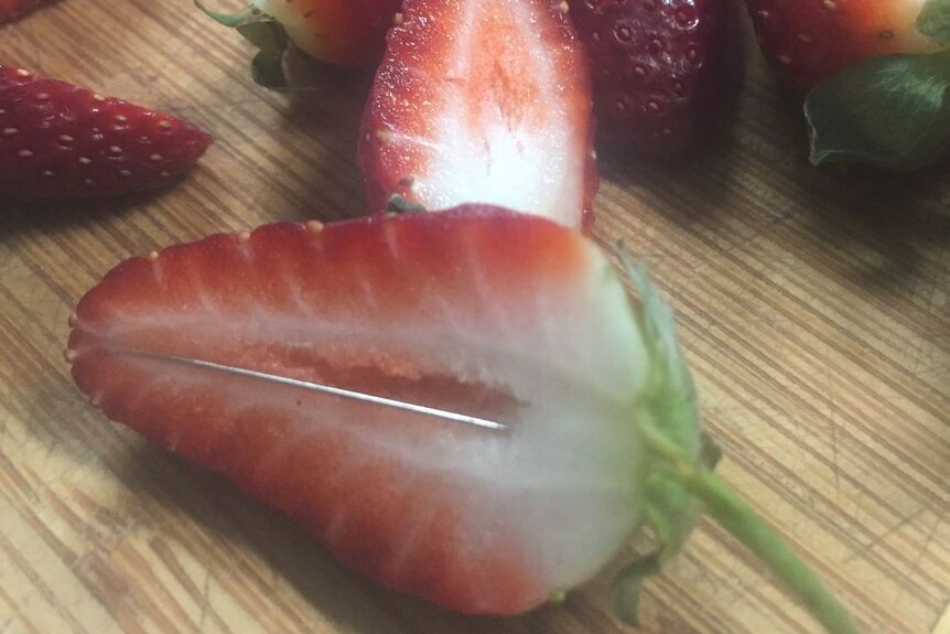 A strawberry cut in half with a needle in it.