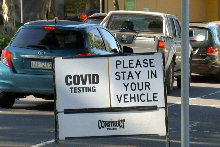 Cars lined up outside a mobile COVID testing station with a sign reading: COVID testing please stay in your vehicle