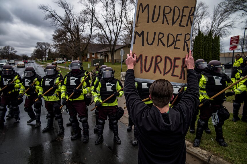 Des manifestants confrontent la police vêtue d'un équipement anti-émeute avec un panneau indiquant "meurtre, meurtre, meurtre".