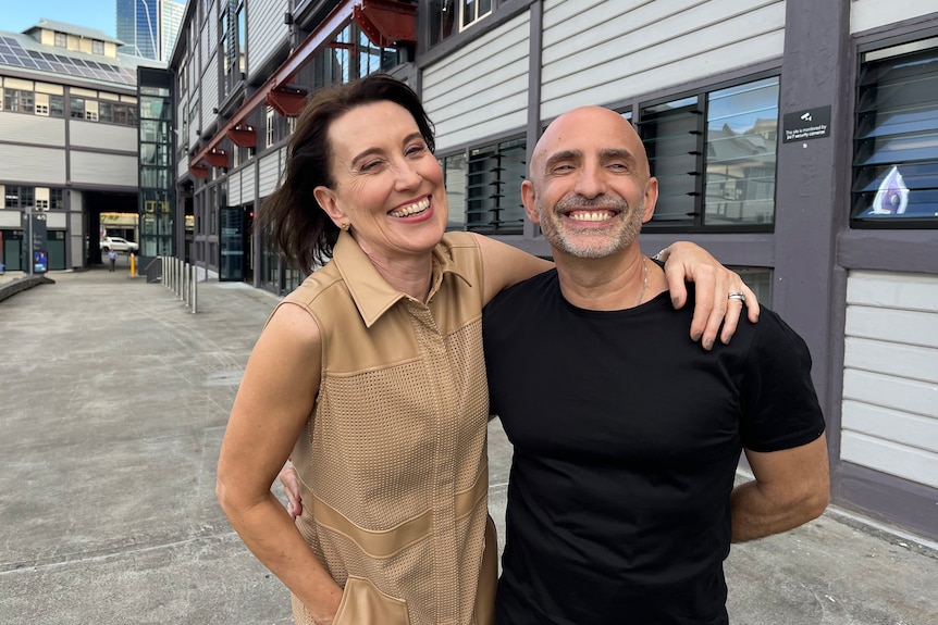 Virginia Trioli and Rafael Bonachela smile brightly, arms around each other, standing on a wharf.