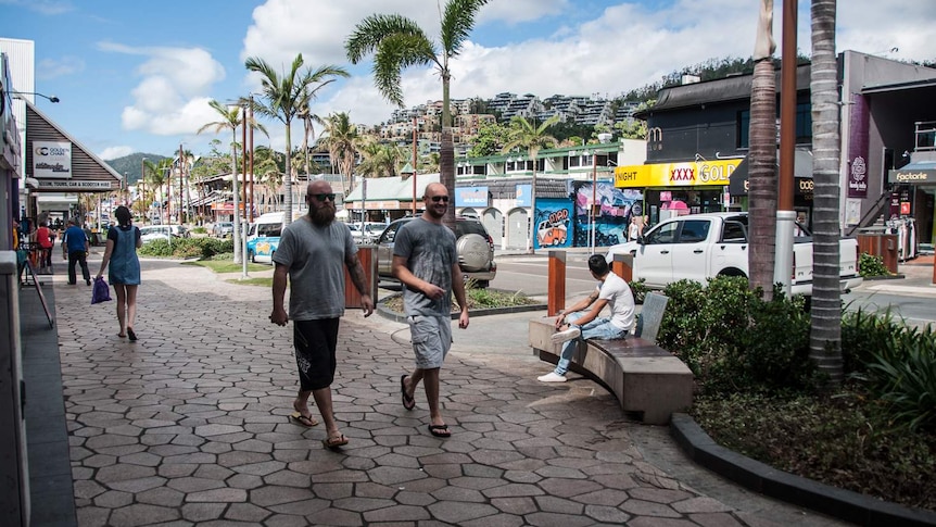 People walking down shopping strip of Airlie Beach main street.