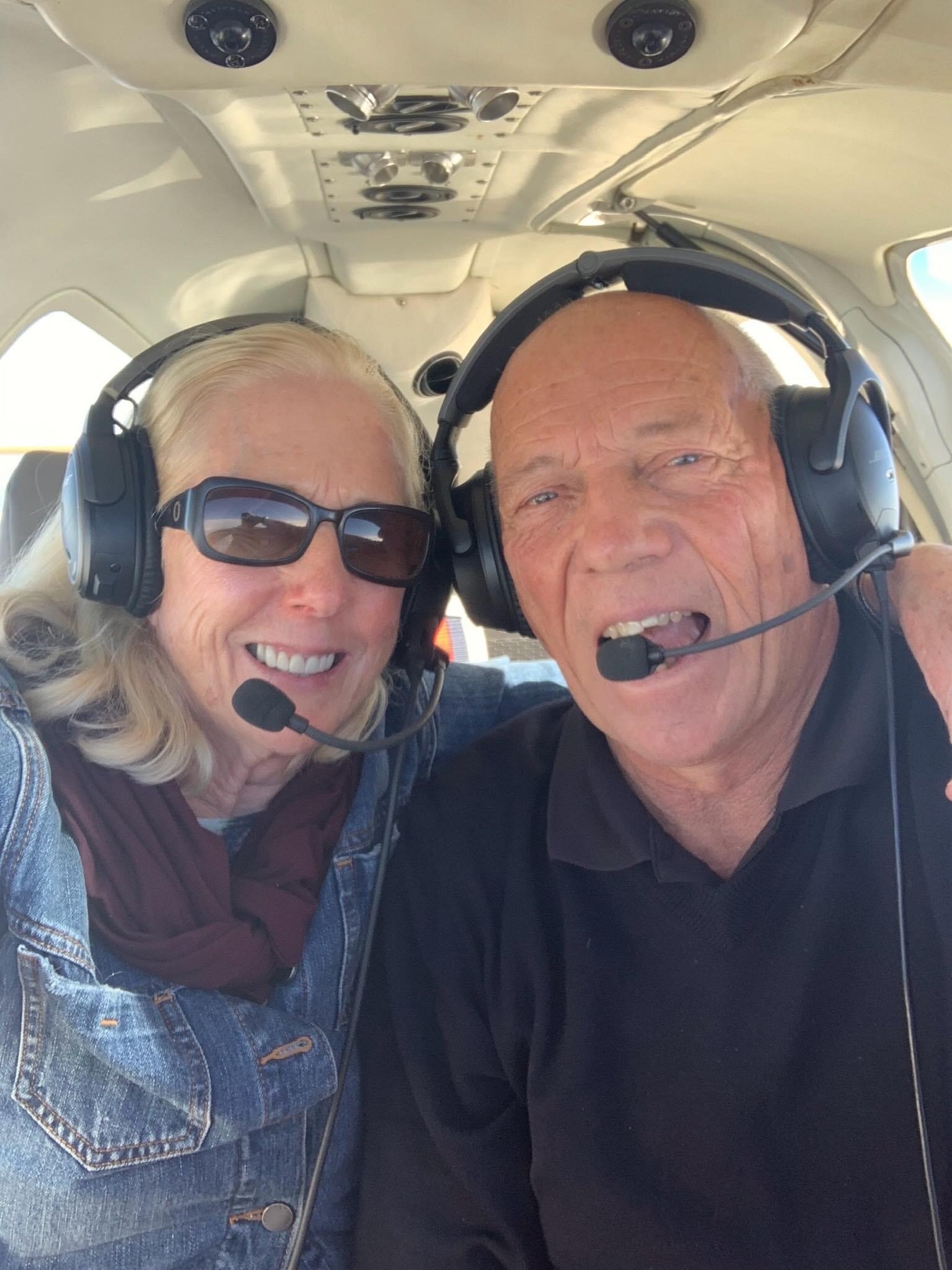 Gary Criddle y una mujer sonríen dentro de una avioneta con auriculares de aviación.