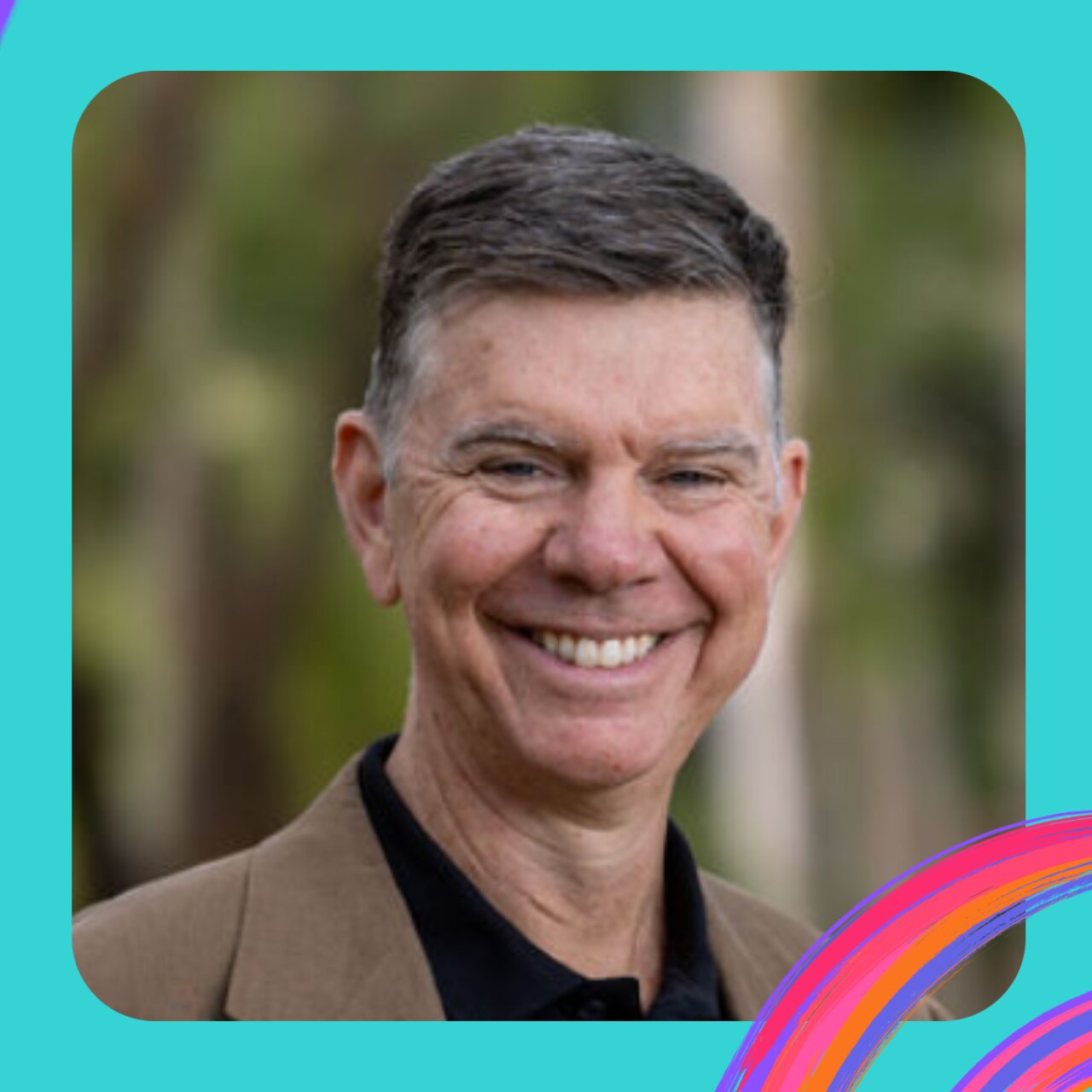 A portrait of David Riley, who wears a tan blazer and black shirt. He is smiling widely and has short grey hair.
