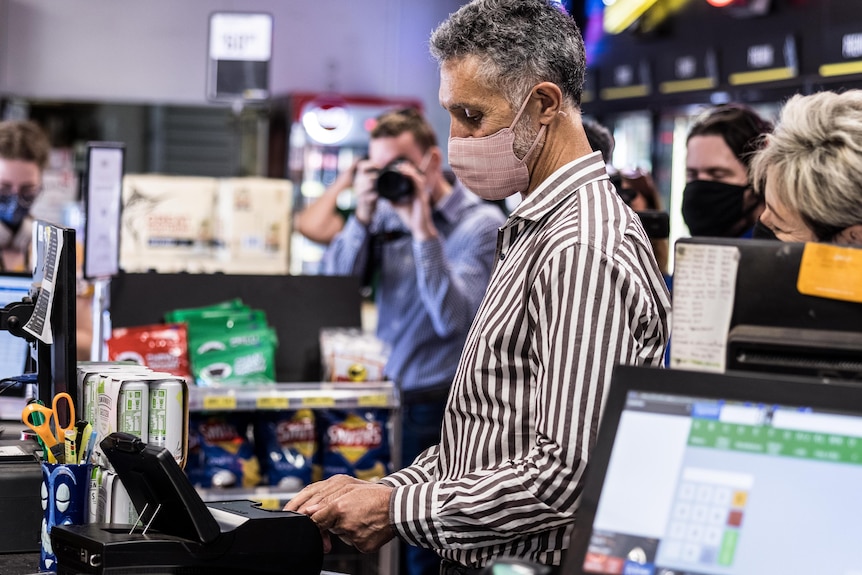 A man wearing a mask scans his ID inside a liquor store. 