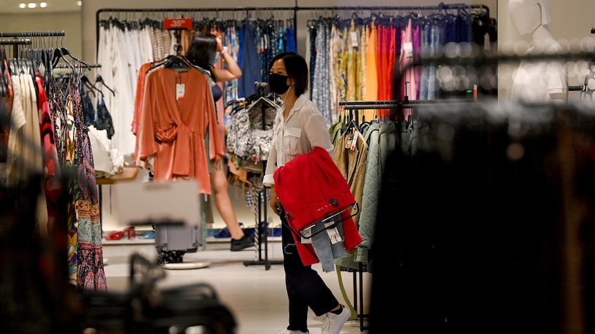 a woman wearing a mask shopping inside a woman's clothing store