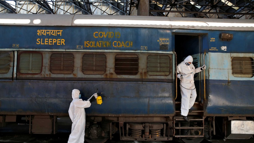 Workers wearing protective suits disinfect the exterior of a passenger train with COVID-19 isolation coach written on it