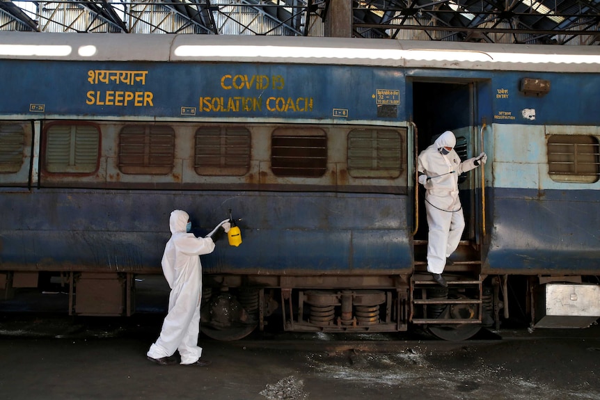 Workers wearing protective suits disinfect the exterior of a passenger train with COVID-19 isolation coach written on it