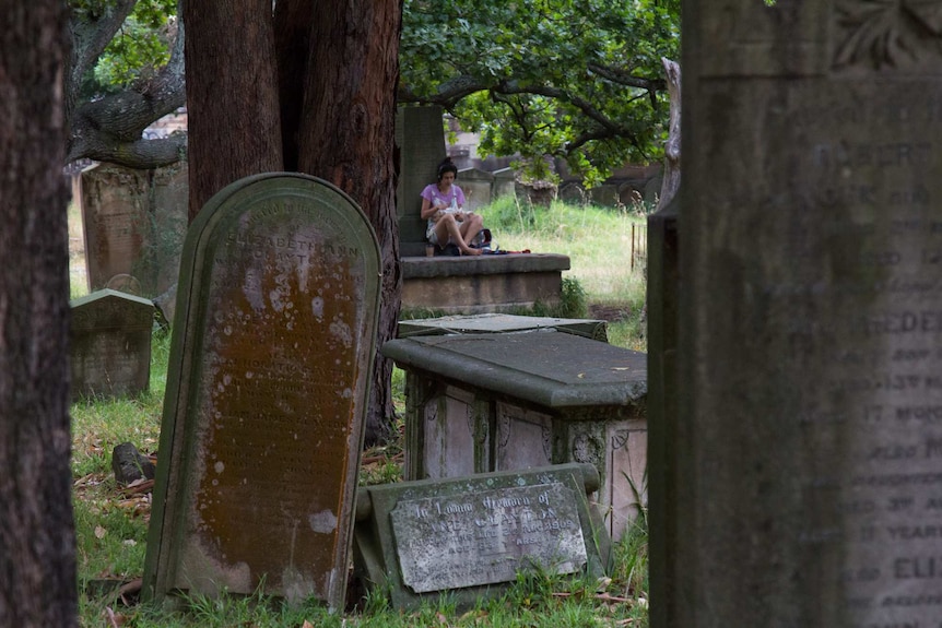 A woman sits on a gravestone in Camperdown cemetery