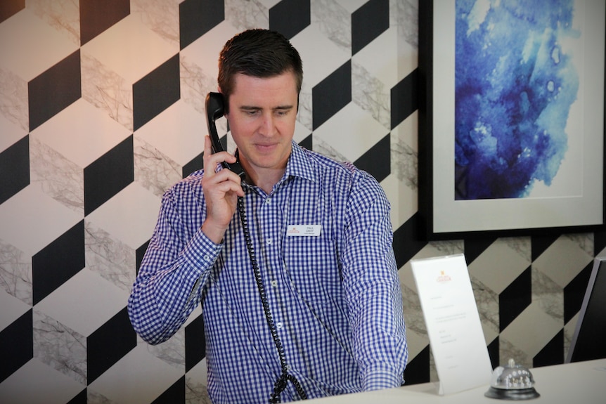 A man answers the phone while standing behind a hotel reception desk