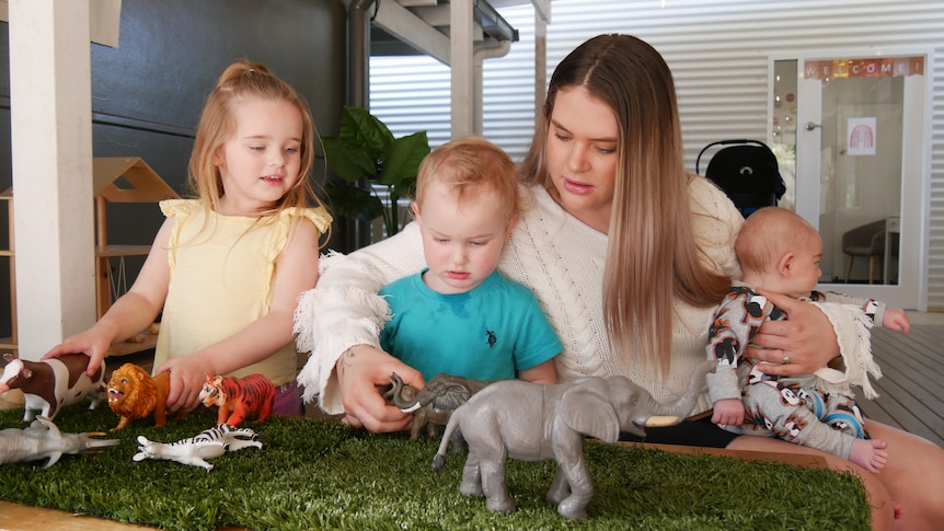 A woman plays with animal toys with her three young children. 