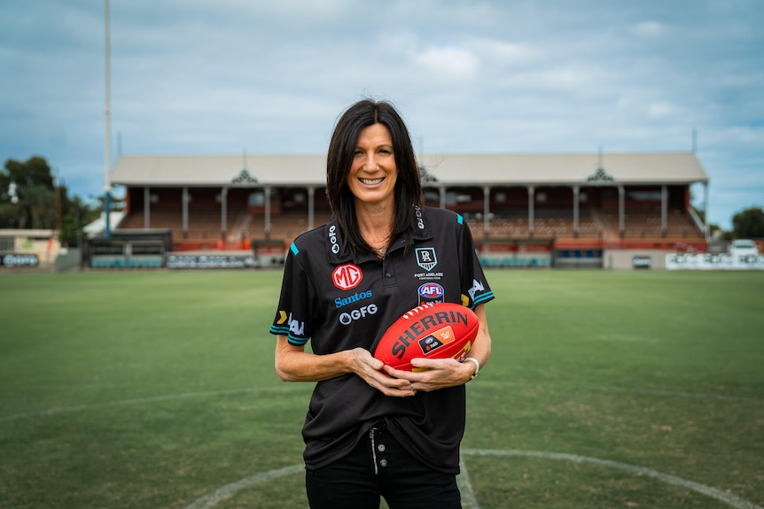 A woman in Port polo shift holding a football on the field.