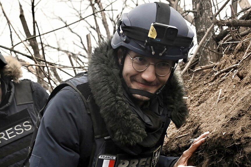 A man in a trench with warm clothes and helmet holding video camera.