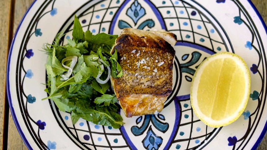 Bird's eye view of crispy-skinned fish on a colourful plate with a herb salad.