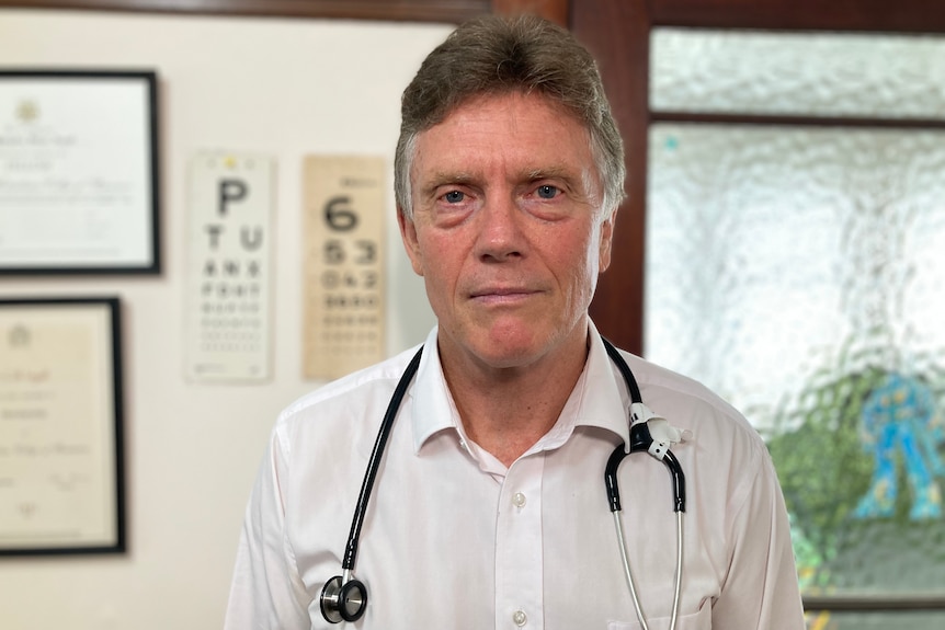 A man in a white business shirt with a stethoscope hanging around his neck looks at the camera.