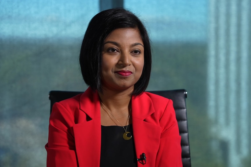 A woman in a red blazer sits in a chair.