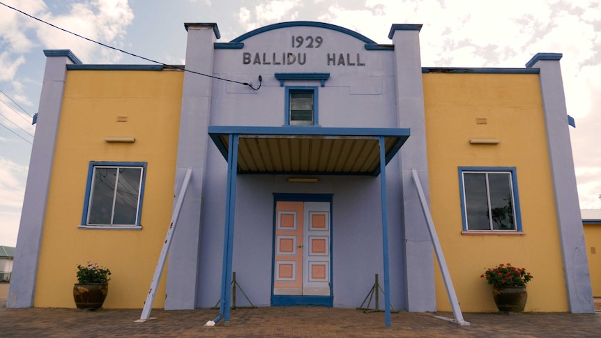 A large blue and white building labelled '1929 Ballidu Hall', blue sky and clouds