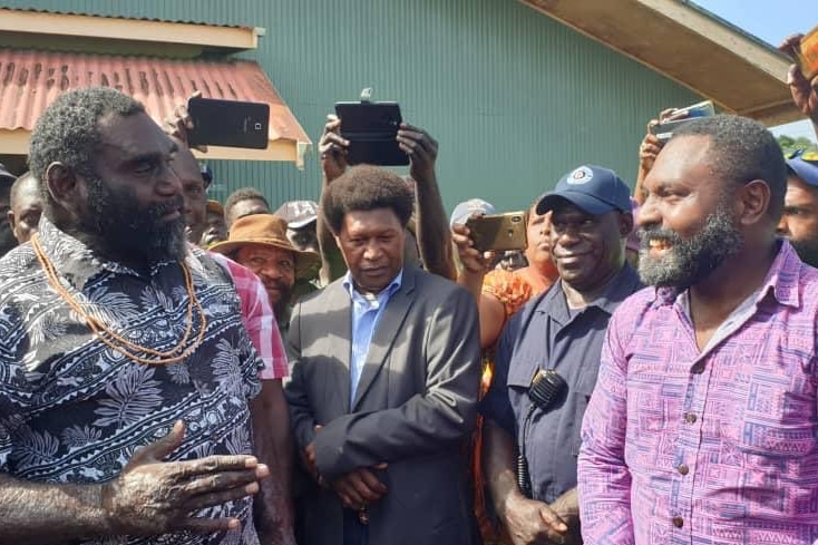 Ishmael Toroama speaks to another man while people film and watch on.