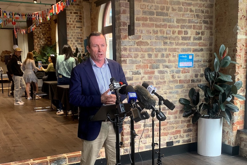 Mark McGowan speaks into microphones with students pictured in the background