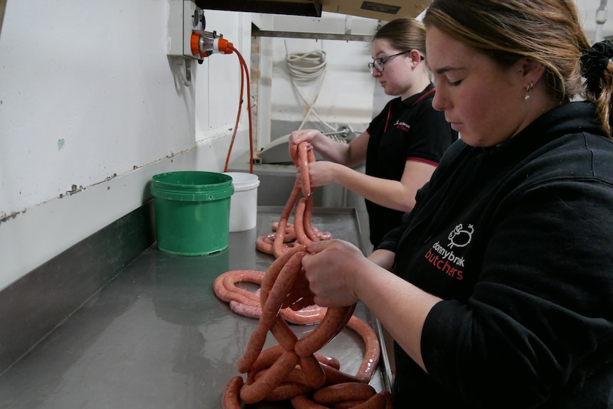 Two girls work in the back of a butcher shop making sausages