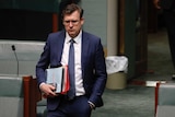 Tudge looking down, left hand in pocket, right hand carrying phone and documents.