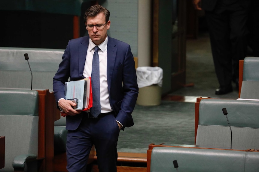 Tudge looking down, left hand in pocket, right hand carrying phone and documents.