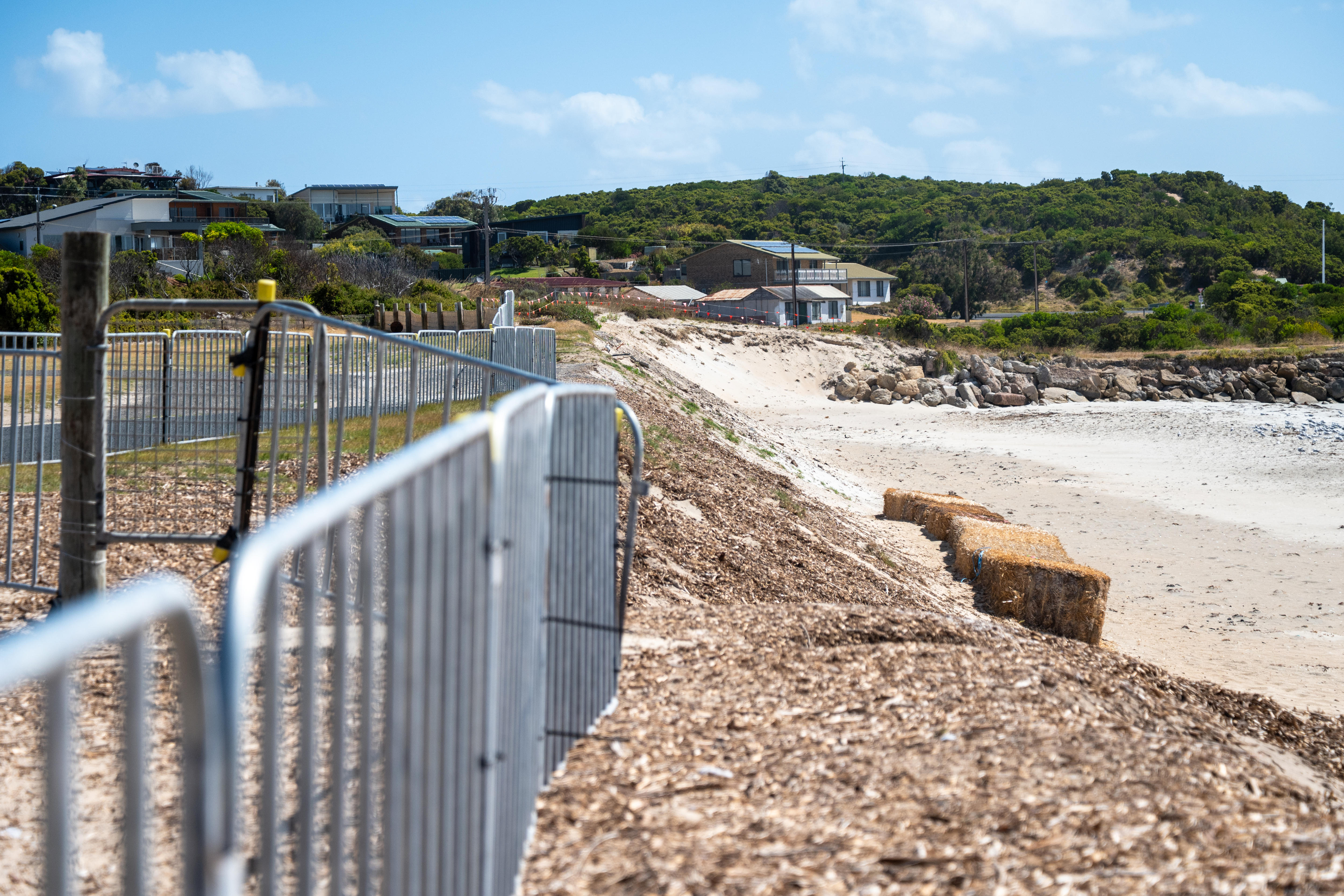 Valla metálica improvisada sobre dunas de arena, incluida la playa y una hilera de fardos de heno.