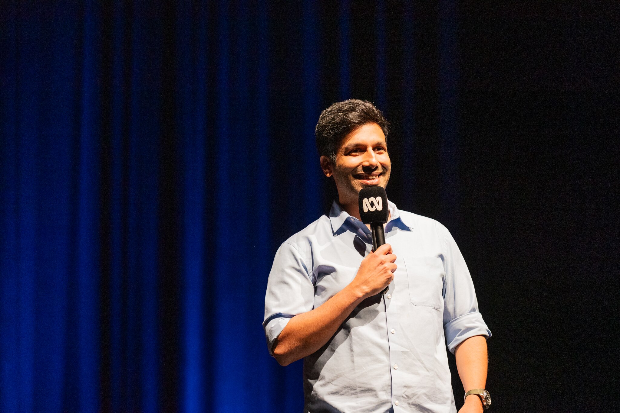 Kanan Gill on stage with dark blue stage curtains in the background.