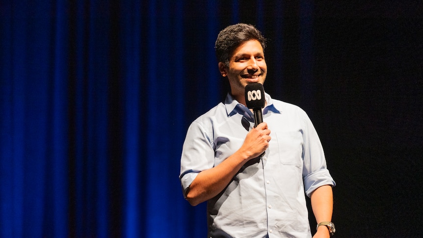 Kanan Gill on stage with dark blue stage curtains in the background.