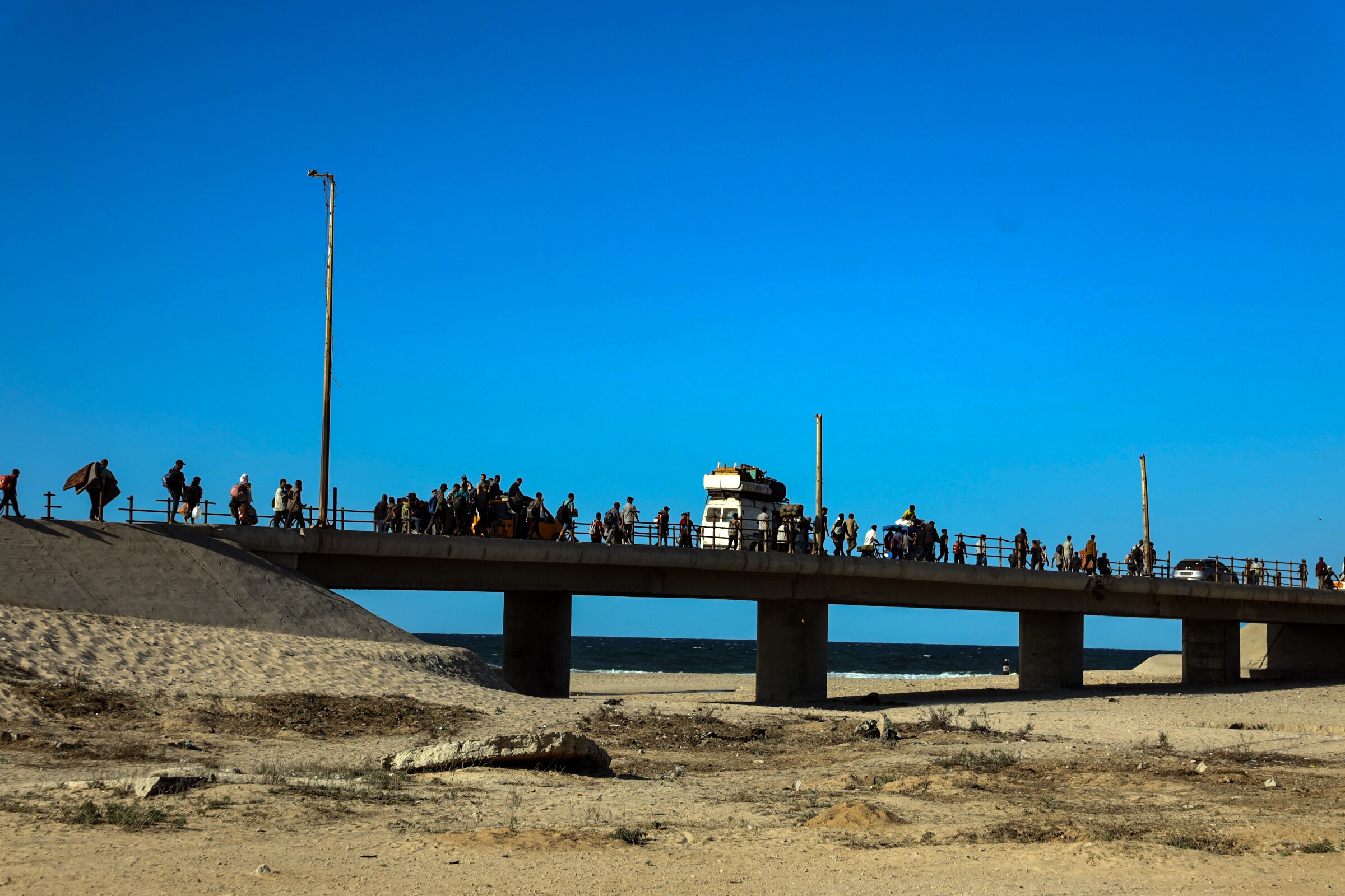 A short bridge connecting sand dunes with people walking on top.