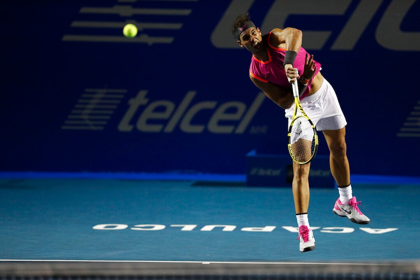 Rafael Nadal pictured in a pink singlet and white shorts having just served a tennis ball on a court with Acapulco written on it