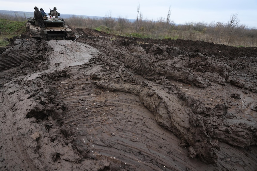 Ukrainian tankers man their positions atop a tank in a muddy field.
