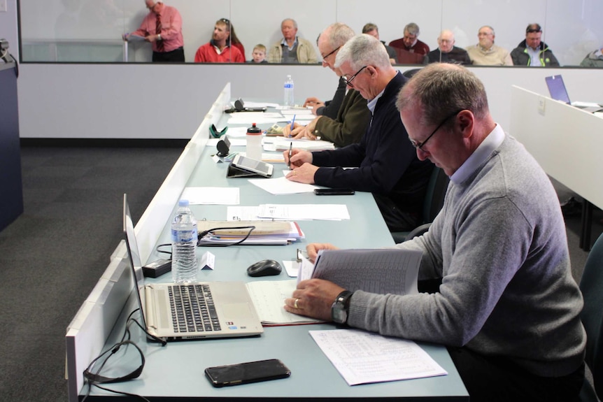 Mean sitting in a room with paper and computers bidding on wool being auctioned.