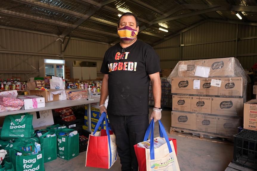 A man in a COVID mask holding grocery bags.