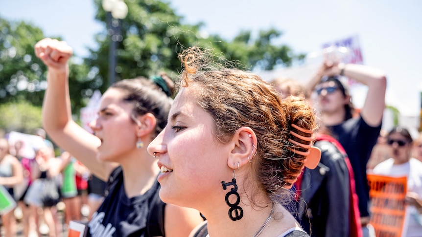 A group of women stand on a street with their fists in the air or holding signs in protest.