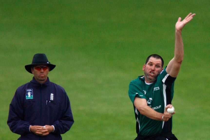 Matt Mason bowls a cricket ball during a match in England with an umpire standing to his right.
