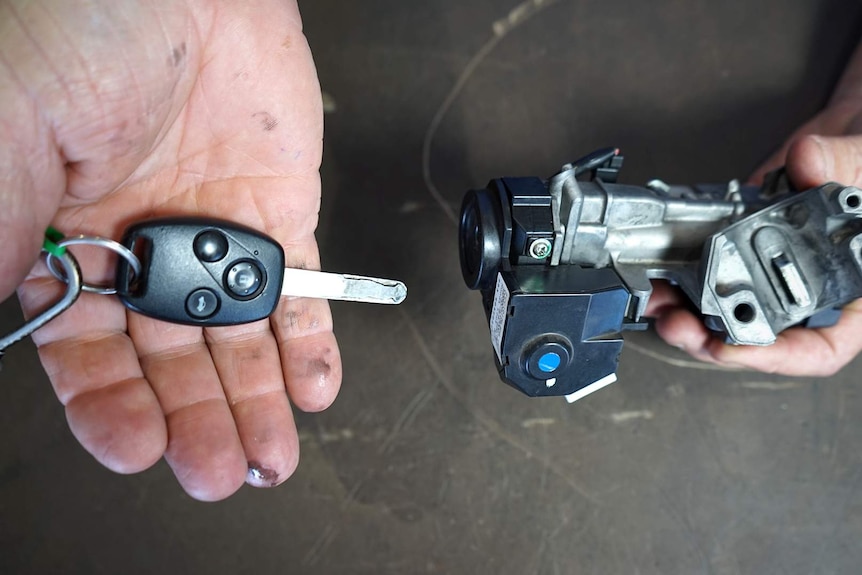Man holds a key in one hand and a motorbike locking system in the other