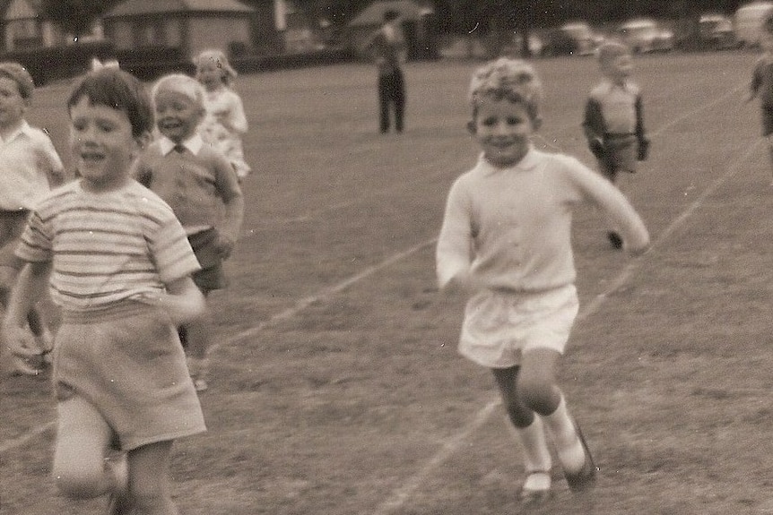 A monochrome of a young smiling boy in a running race wearing school uniform.