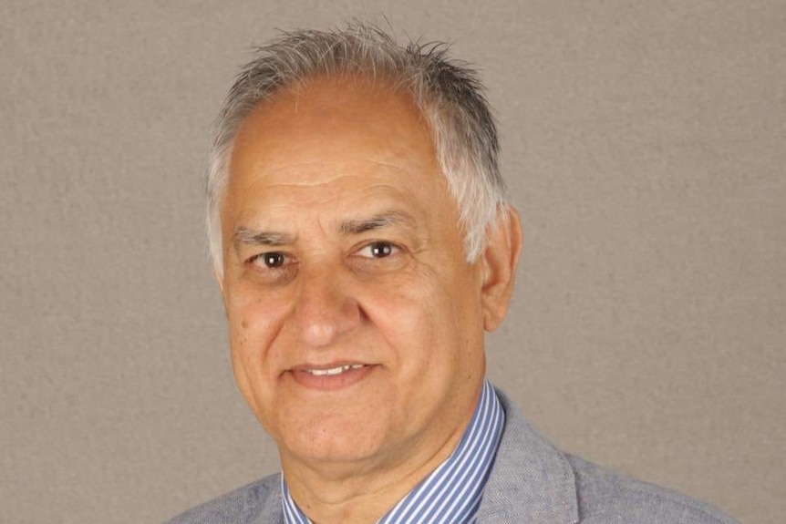 A man with grey hair, wearing a pale suit, shirt and tie, smiling.