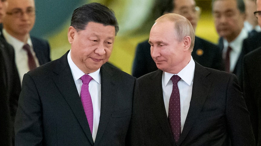 Xi Jinping dressed in a suit with a pink tie leans his heads towards a smiling Vladimir Putin.