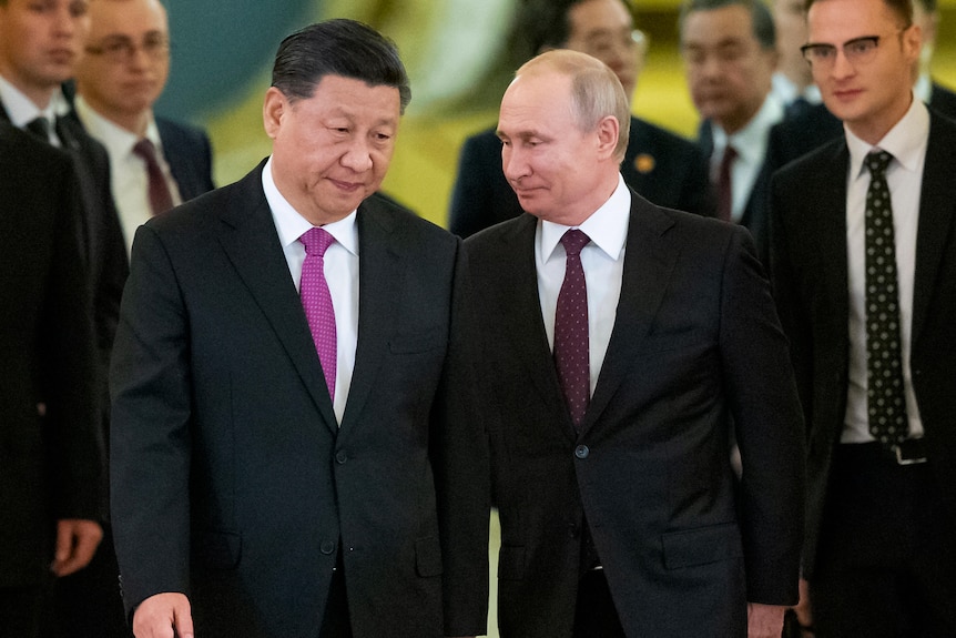 Xi Jinping dressed in a suit with a pink tie leans his head towards a smiling Vladimir Putin.